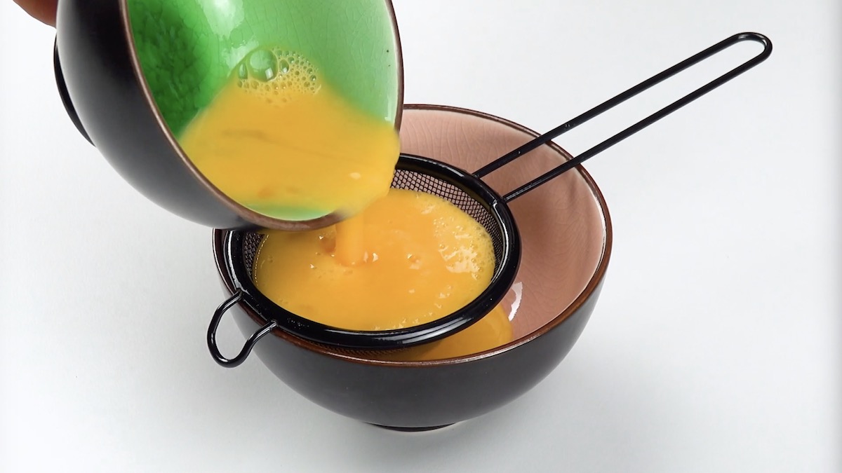 Verquirlte Eier werden durch Sieb in Schüssel geseiht