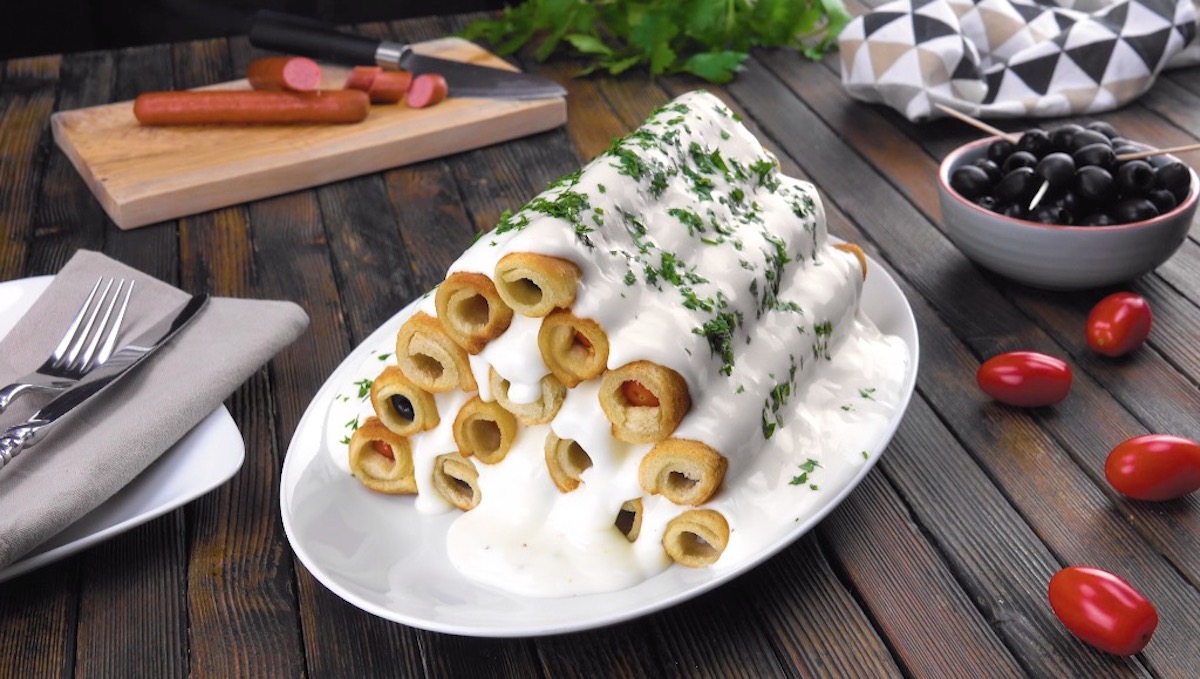 Pyramide aus gefüllten Toaströllchen, die mit Käsesoße übergossen und mit Petersilie garniert wurde