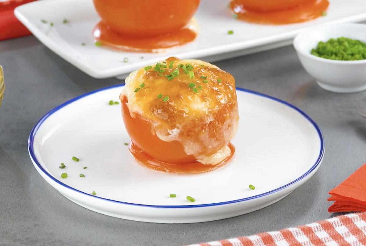 Ein Tomaten-Ei mit überbackenem Käse und gehacktem Schnittlauch auf einem Teller