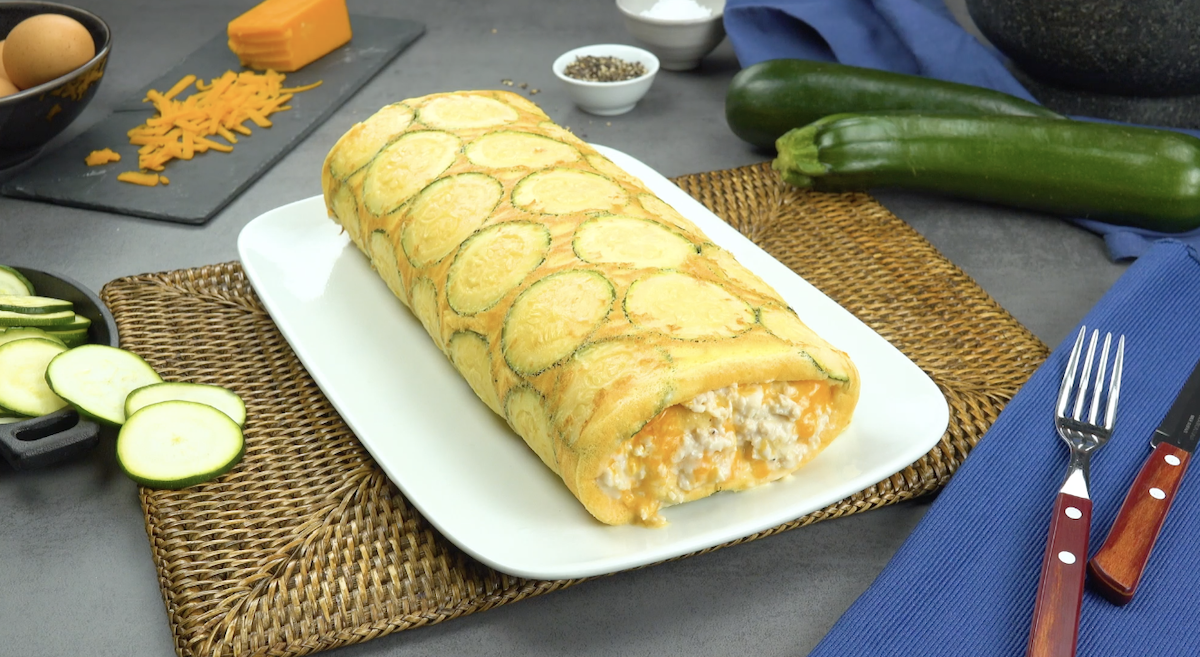 Zucchini-Omelett-Rolle mit Füllung aus Cheddar und Hähnchen auf weißem Teller
