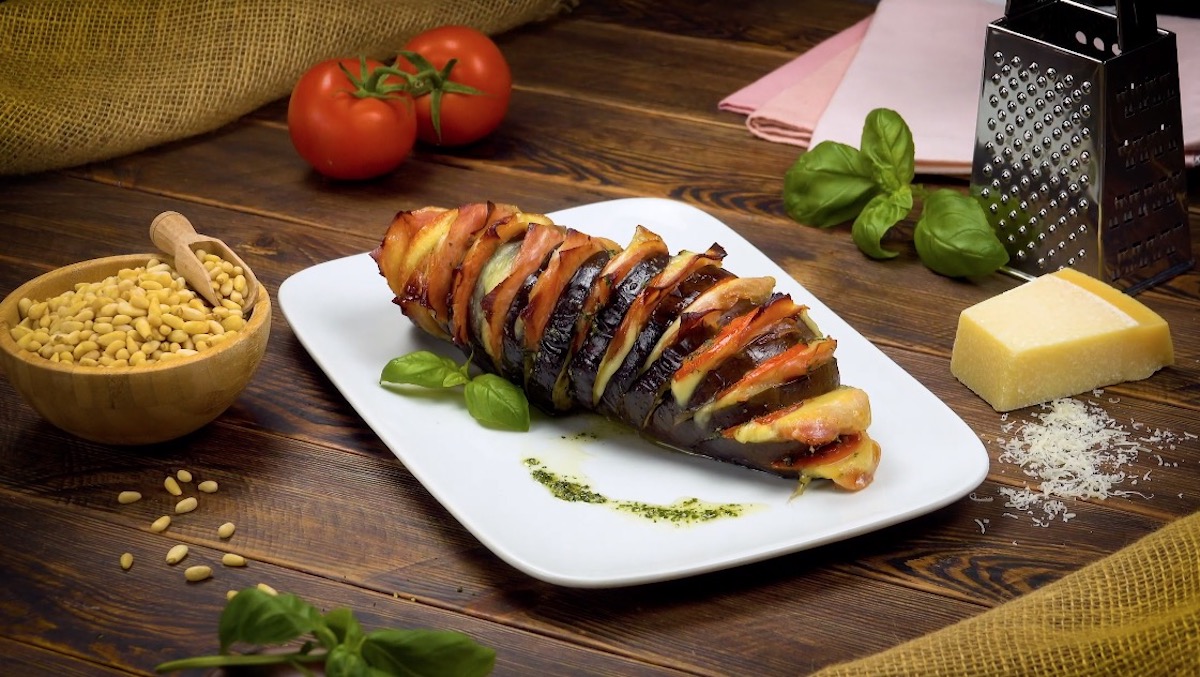 Aubergine à la Hasselback, mit Kochschinken und Tomaten gefüllt, auf weißem Teller