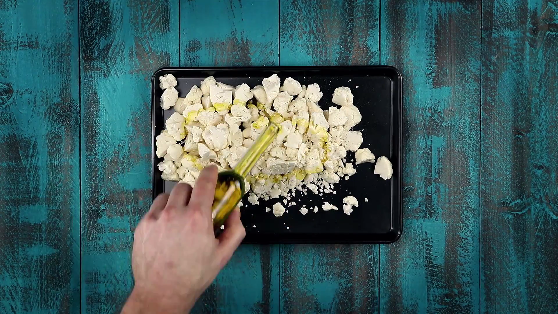 Zerkleinerter Blumenkohl auf Backblech wird mit Öl übergossen