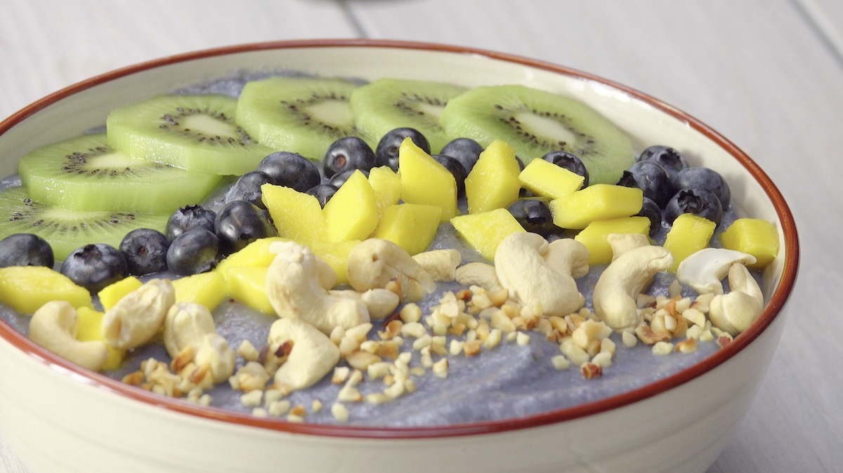 Smoothie-Bowl mit Kiwis, Blaubeeren, Mangostücken und Cashew- und Haselnüssen
