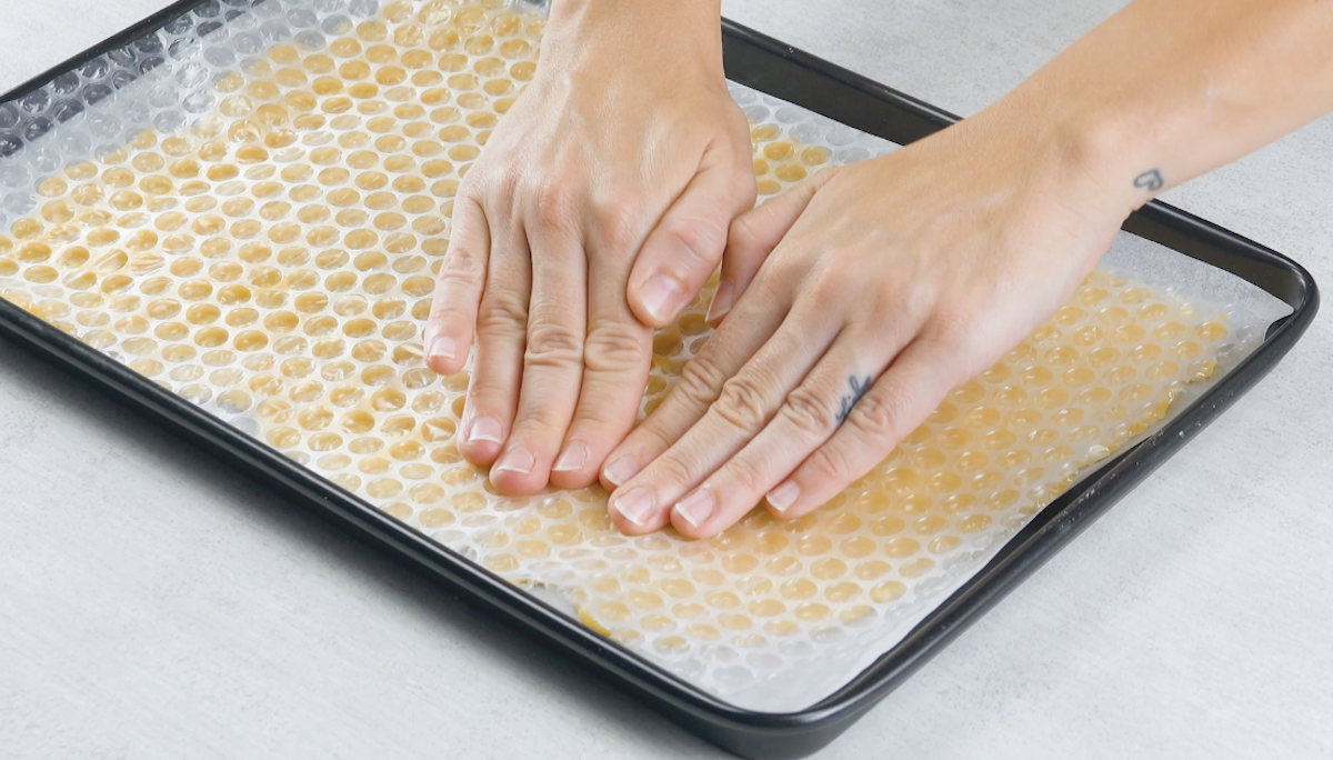 Luftpolsterfolie wird auf Keksteig, der auf mit Backpapier belegtem Blech liegt, gedrückt