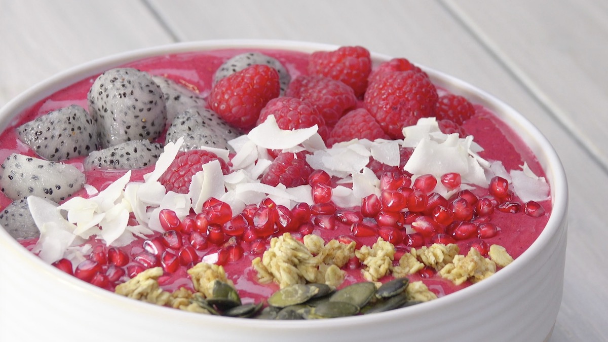 Smoothie-Bowl mit Himbeeren, Drachenfrucht, Granatapfelkernen, Müsli und Kürbiskernen