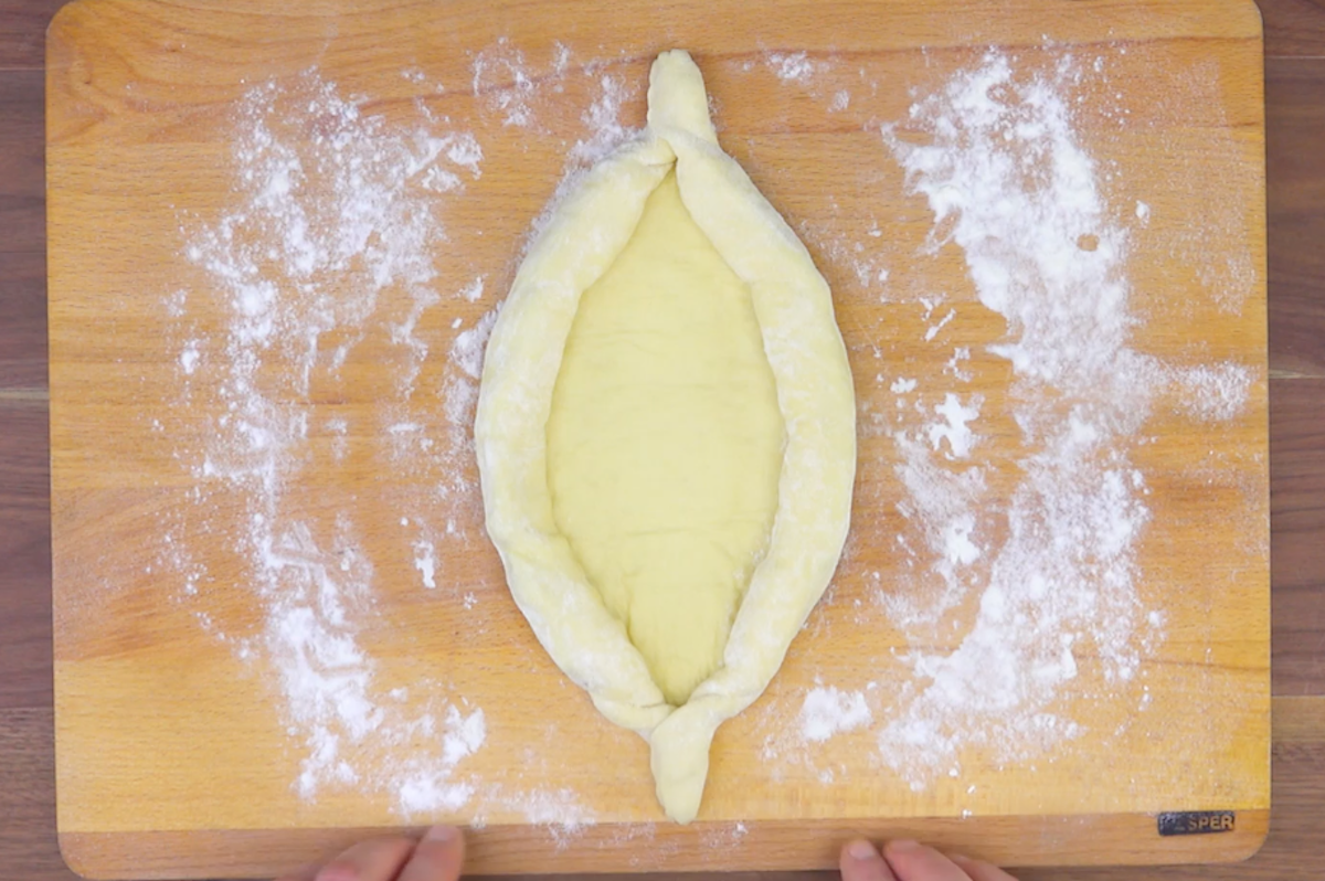 Der Teig wird über den Mozzarella zur Mitte hin eingerollt, sodass ein Schiffchen entsteht