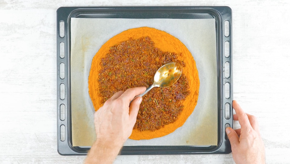 Rotes Pesto wird auf Pizzateig aus Butternutkürbis verteilt