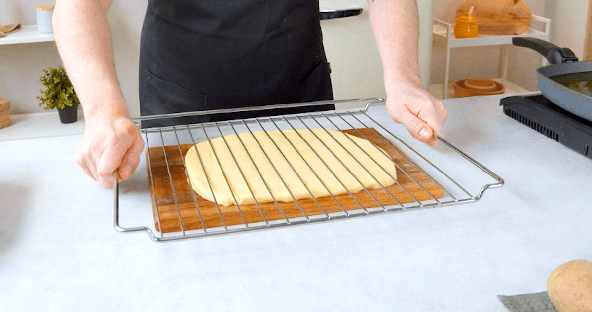 Jemand drÃ¼ckt einen Ofenrost auf eine flach ausgewalzte Schicht Kartoffelbrei.