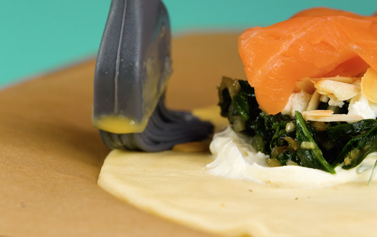 Die Teigränder des Pizzateigs werden mit verquirltem Ei bestrichen.