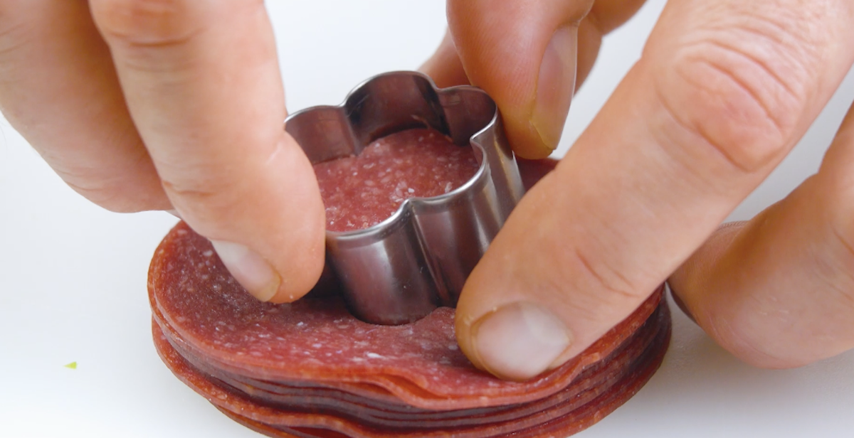 Salamischeiben werden mit Plätzchenausstecher in Blumenform ausgestochen