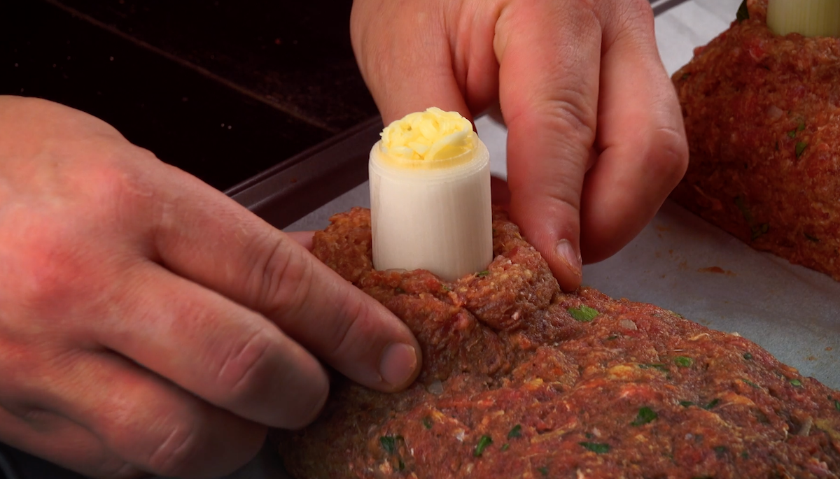 Ein mit Käse gefülltes Lauchstück wird in Hackfleisch gedrückt