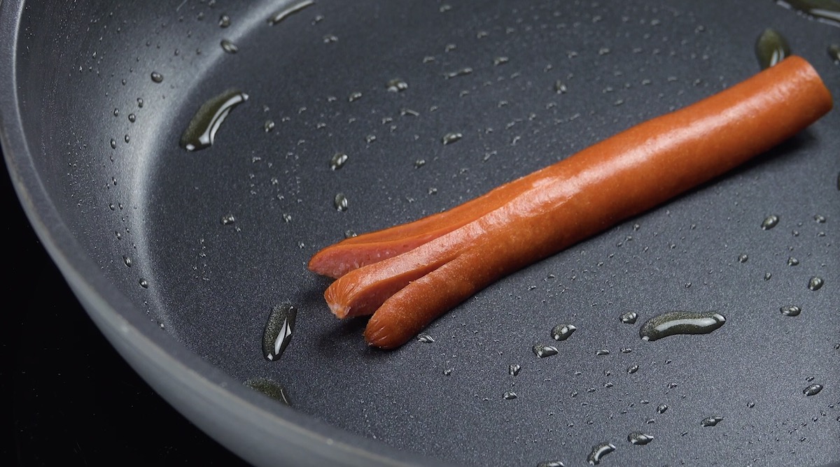 Halbiertes Würstchen, das am Ende eingeschnitten wurde, in Pfanne mit Öl