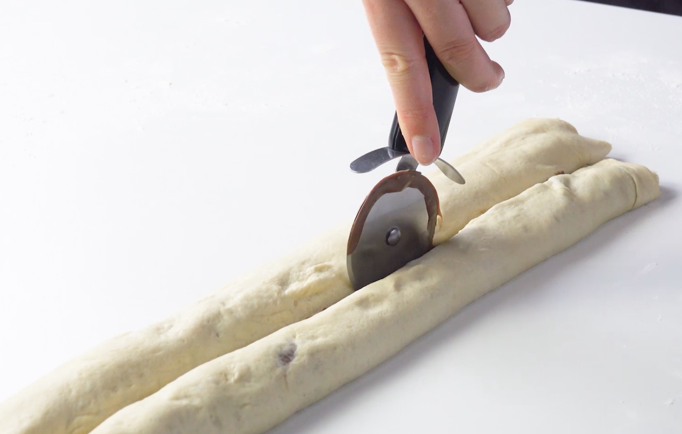 Hefeteigrollen werden mit einem Pizzaschneider längs in der Mitte durchgeschnitten.