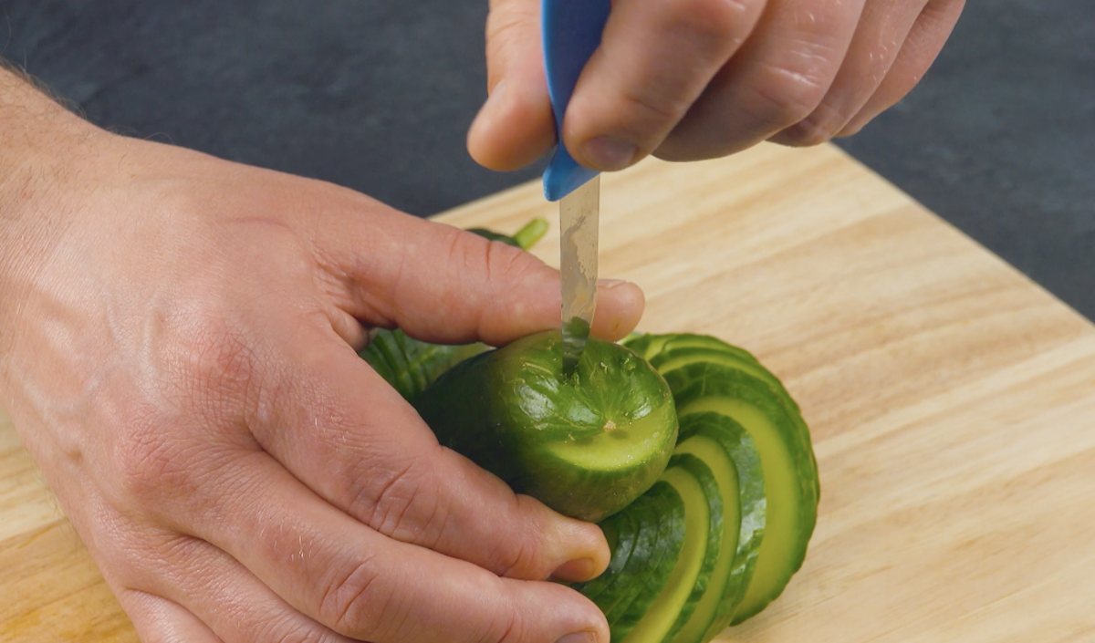 Mit Messer werden Löcher für Augen und Mund in Gurke geschnitten