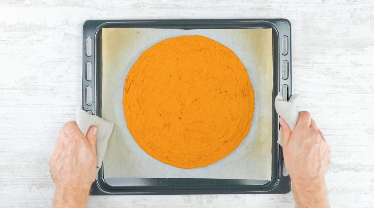 Runder Pizzateig aus Butternutkürbis auf Blech mit Backpapier