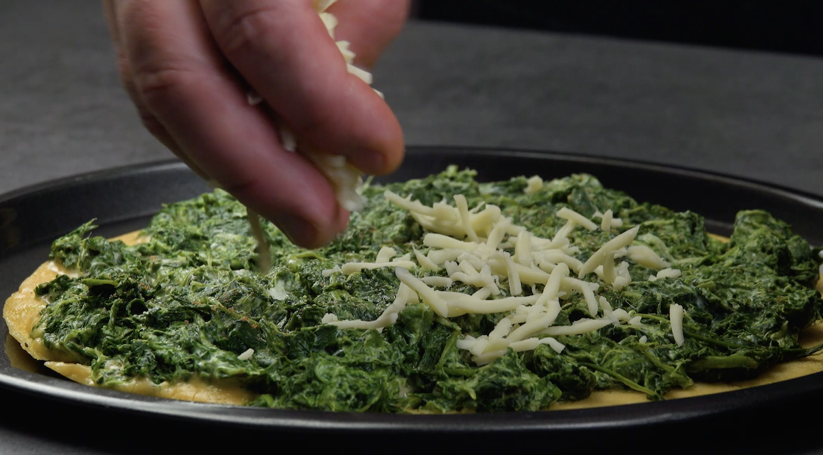 Spinat-Frischkäse-Mischung auf Omelett-Pfannkuchen wird mit geriebenem Käse bestreut