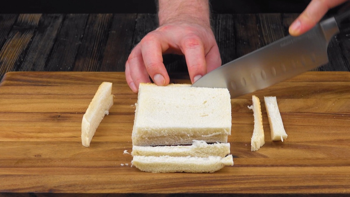 Von zwei übereinander gelegten Toastbrotscheiben wird die Rinde abgeschnitten