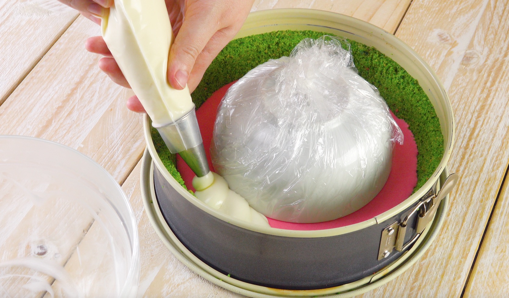 Eine in Frischhaltefolie eingewickelte Schüssel wird kopfüber in die Mitte der Torte gestellt und diese ringsherum mit Creme aufgefüllt