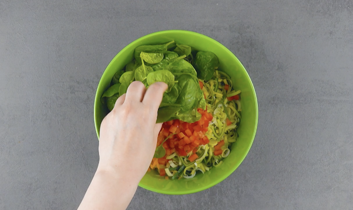 Geriebene Kartoffel und Karotten in Schüssel mit kleingeschnittenem Lauch, Paprika und Spinat