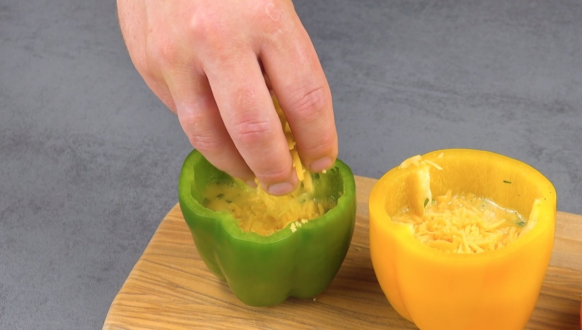 Geriebener Käse wird zu Rührei in Paprikaschote gegeben