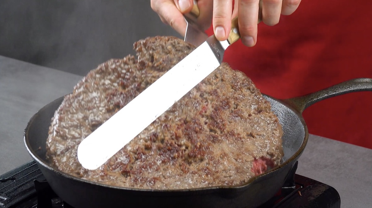 Pfannengroßes Hackfleisch-Patty wird in Pfanne angebraten