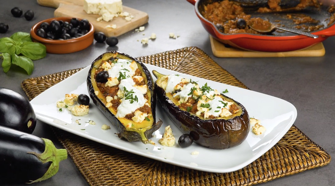 2 mit Hackfleishc und Feta gefüllte Auberginenschiffchen auf weißem Teller