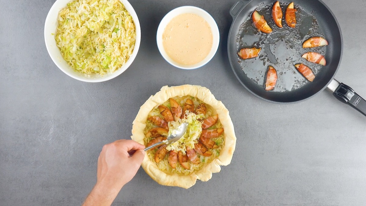 Klein geschnittener Wirsing wird in eine Springform mit Pizzateig und Apfelschnitze gefüllt