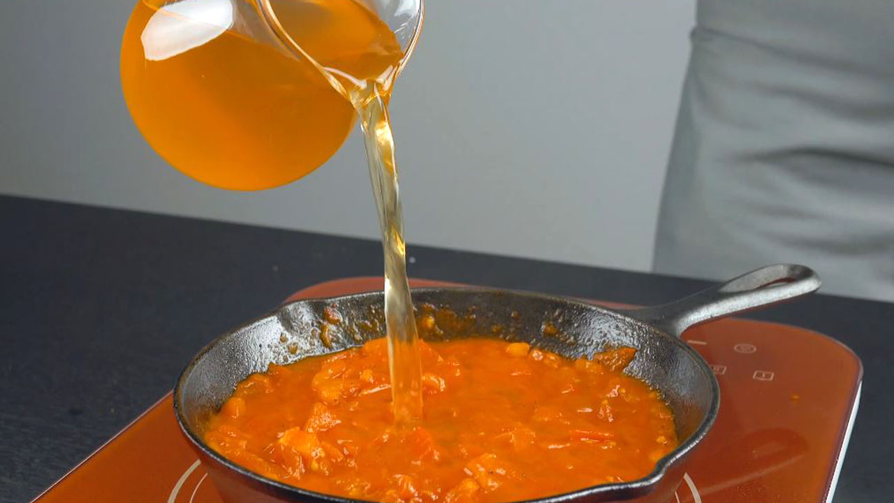 Gemüsebrühe wird in Pfanne mit Tomaten und Gewürzen gegossen