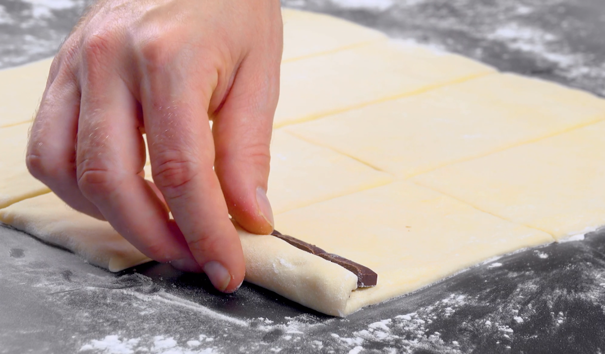 2 längliche Schokoladenstücke werden in ein Rechteck-Stück Teig eingerollt