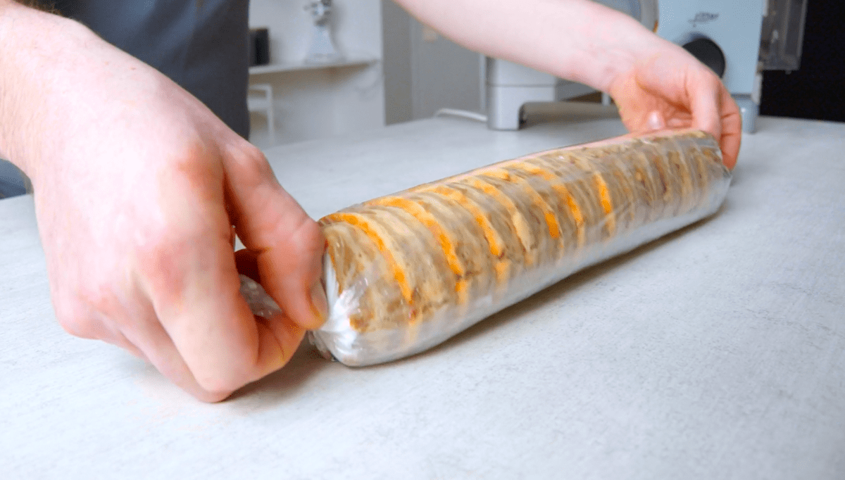Eine süße Brotrolle wird mithilfe von Frischhaltefolie zusammengerollt.