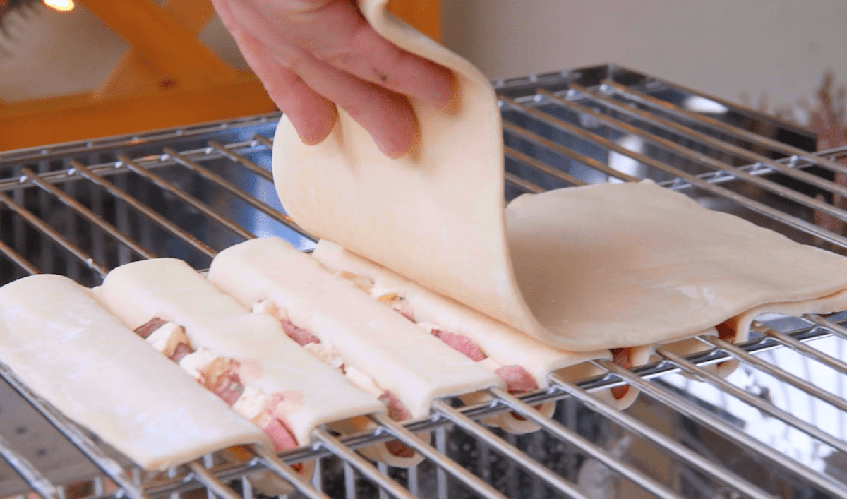 Pizzateig wird auf mit Fleisch-Käse-Spießen belegten Pizzateig gelegt
