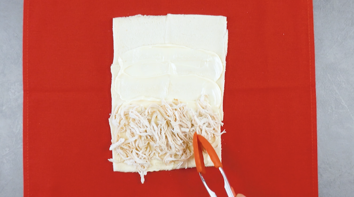 Toastscheiben werden mit Mayo bestrichen und kleingerupftes Hähnchen auf das unterer Drittel gelegt