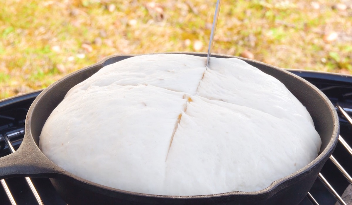 Brotteig in Pfanne auf Grill wird kreuzförmig eingeschnitten
