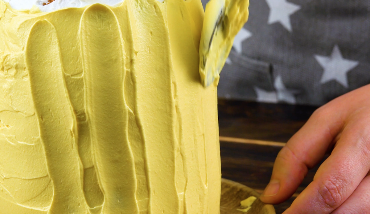 Der Kuchen wird mit gelber Frischkäsecreme ummantelt