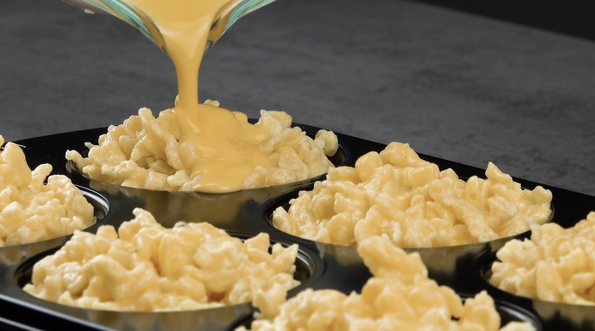 Käse wird über Spätzle in einer Muffinform gegossen