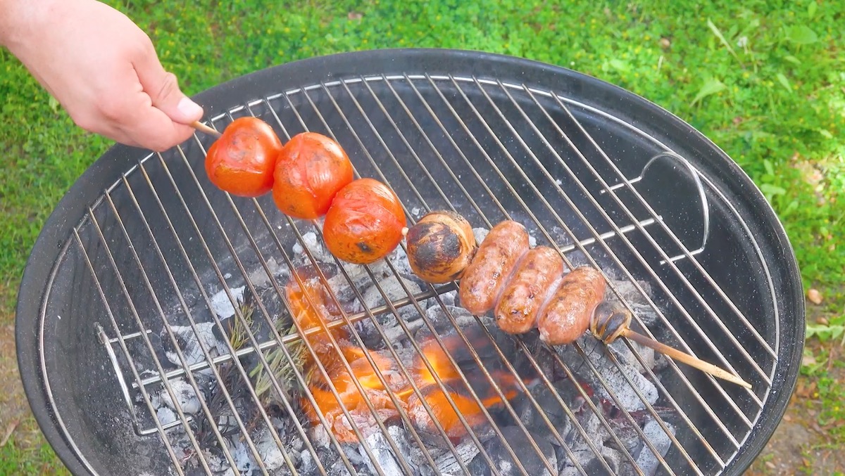 Salsiccias, Zwiebel und Tomaten auf Holzspieß werden auf Grill geröstet