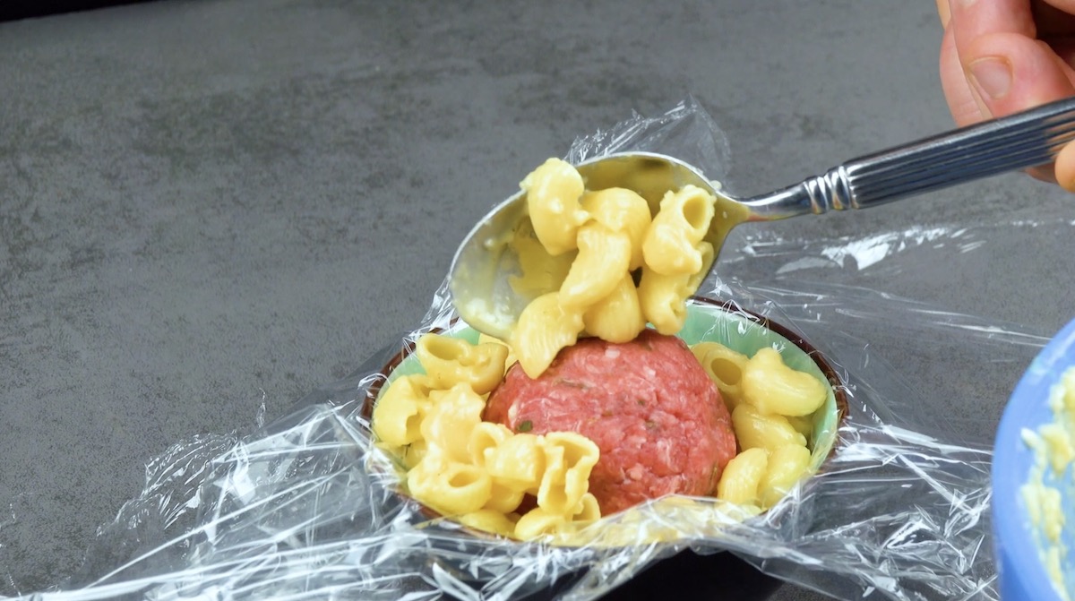 Eine mit Frischhaltefolie ausgekleidete Schüssel wird mit Käsenudeln und Hackbällchen gefüllt.