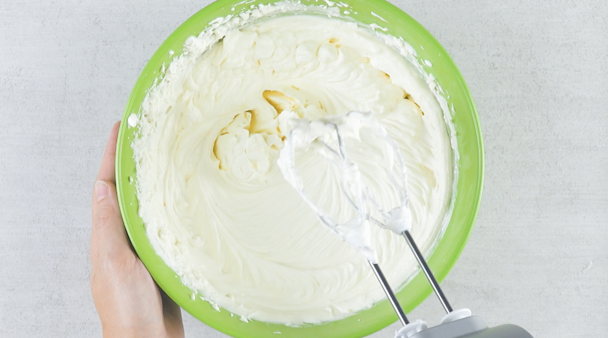 Mascarponecreme wird mit Handrührgerät in Schüssel aufgeschlagen