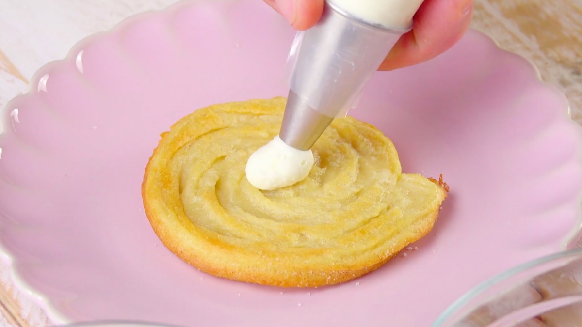 Frischkäsecreme wird mithilfe von Spritzbeutel auf Churro verteilt
