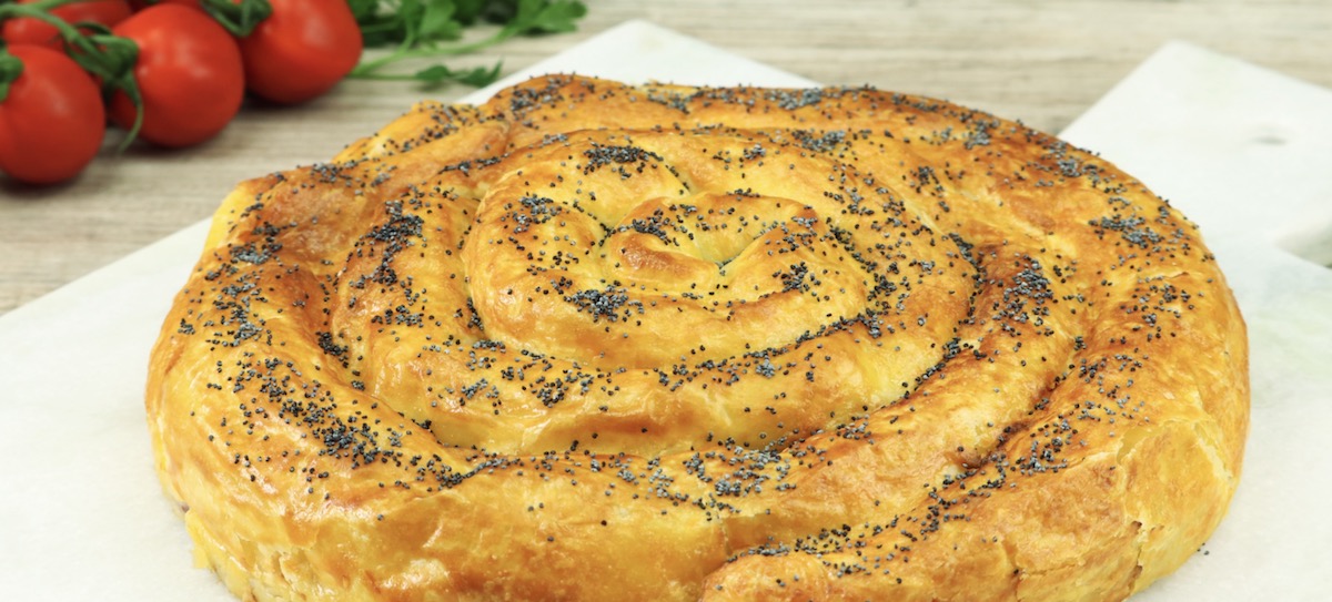 Ein Blätterteigkreisel mit Mohn. Im Hintergrund kleine Tomaten.