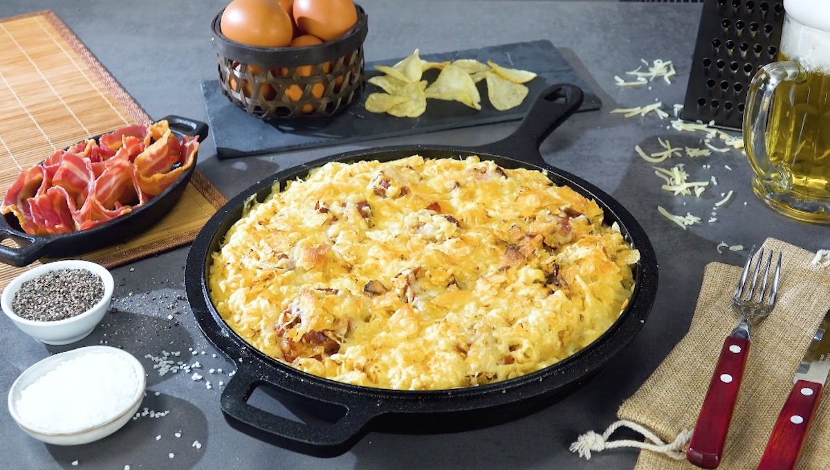 Omelett mit Bacon, Krakauer Würstchen, Chips und geriebenem Käse in Pfanne