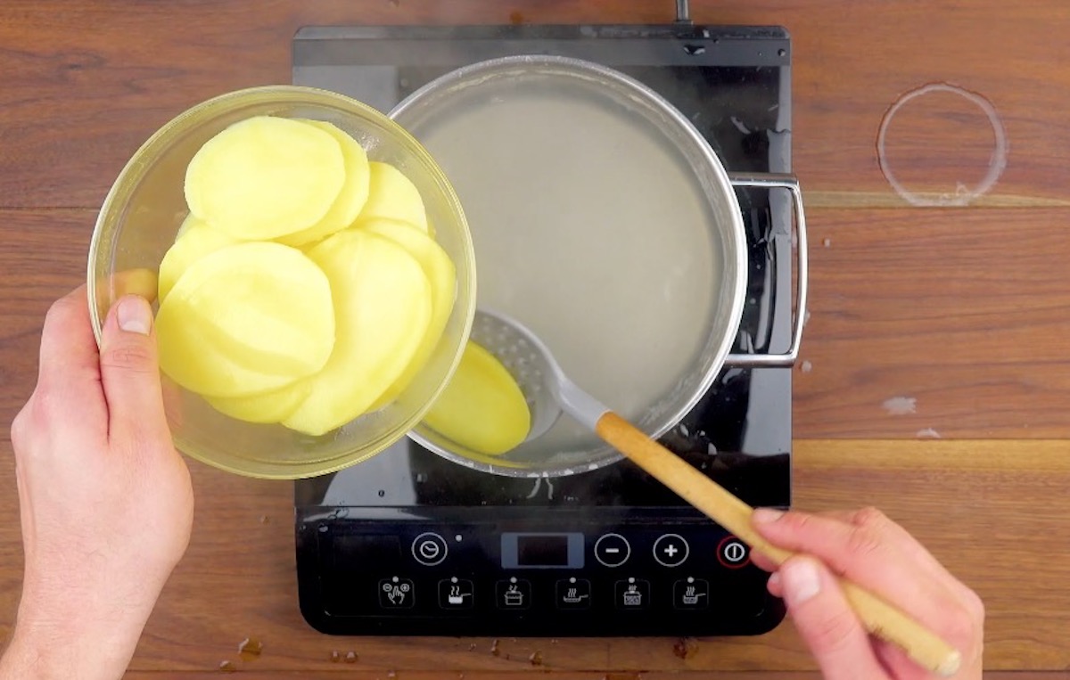 Kartoffelscheiben werden in heißes Wasser in einen Topf gelegt