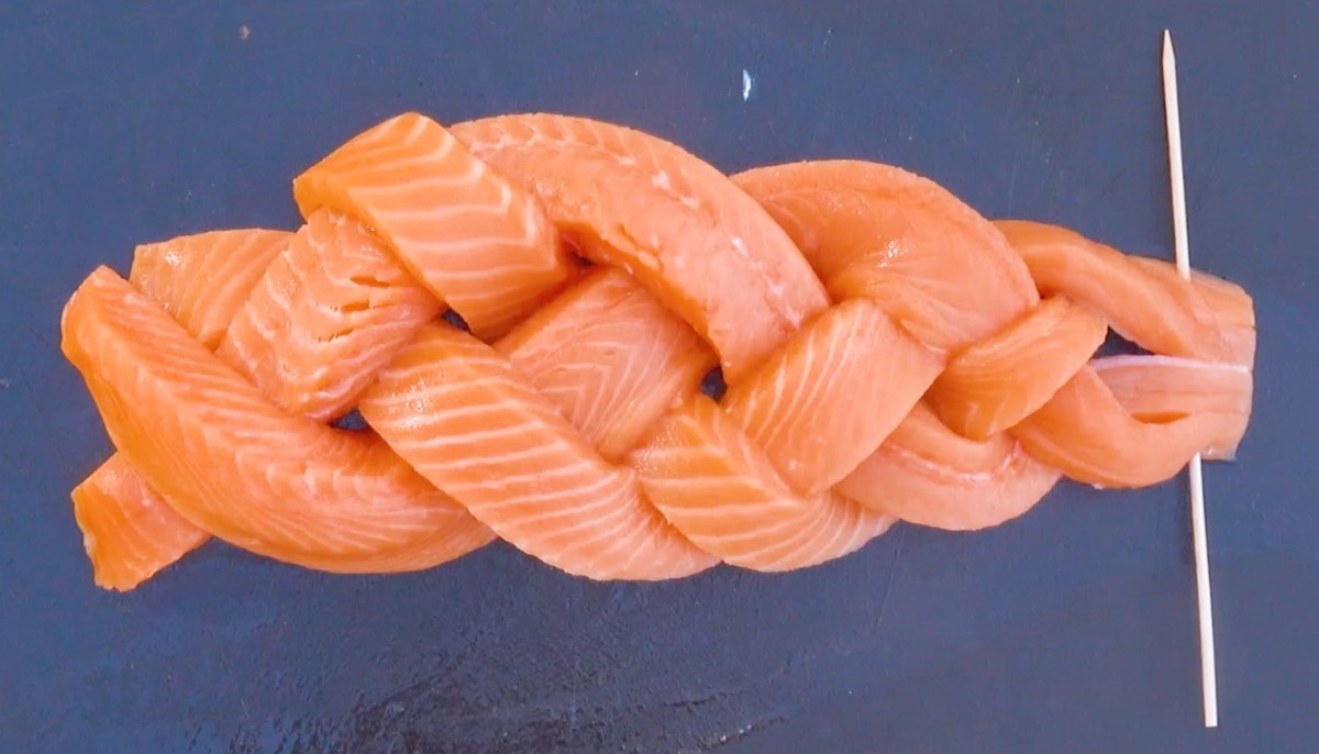 Lachsscheiben werden zu Zopf geflochten und am Ende mit Holzspieß fixiert