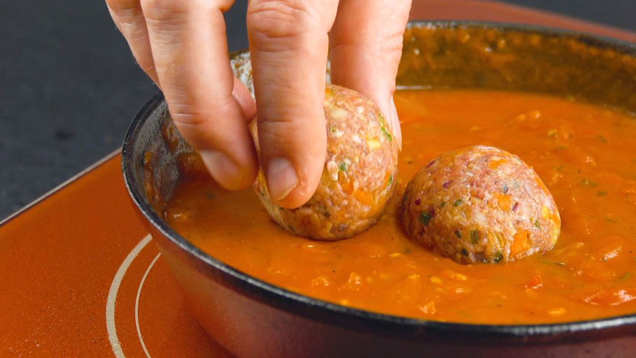 Hackbällchen werden in Tomatensoße in Pfanne gelegt