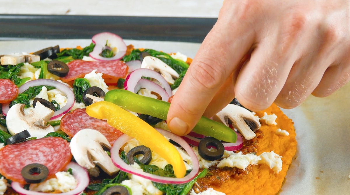 Paprikastreifen in Grün und Gelb werden auf Kürbis-Pizza gelegt