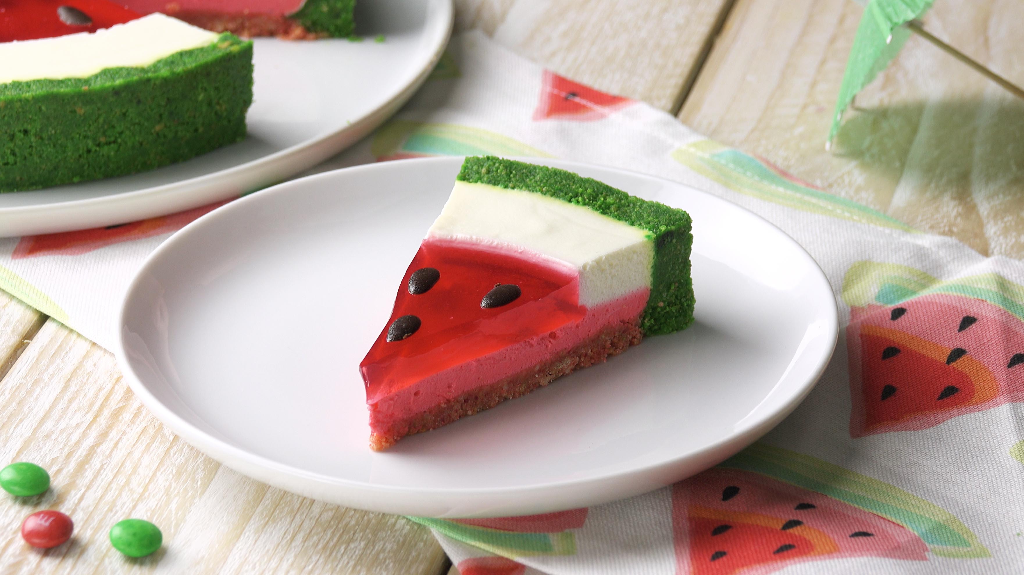 Ein Stück Wassermelonen-Torte auf einem Teller mit der Torte im Hintergrund