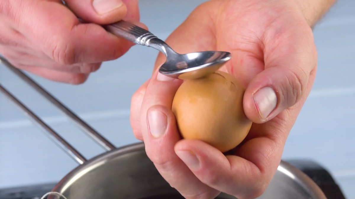 Gekochtes Ei wird mit Löffel rundherum sanft angeschlagen