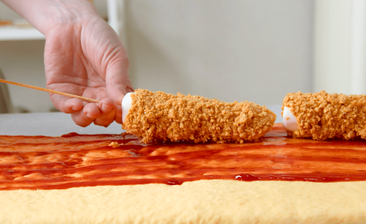 Marshmallows mit Erdnussbutter und klein gehackten Erdnüssen werden auf einen Teig mit Erdbeermarmelade gelegt