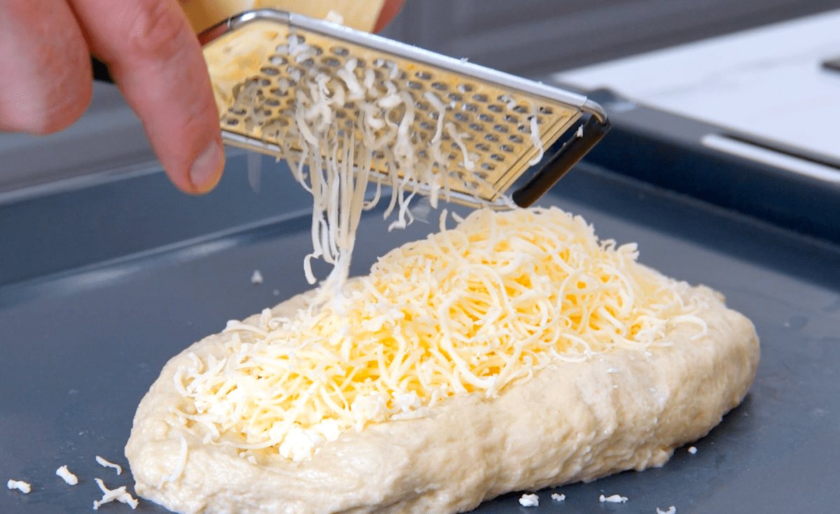 Feta und geriebener Gouda werden auf ein Stück Hefeteig mit Würstchen verteilt