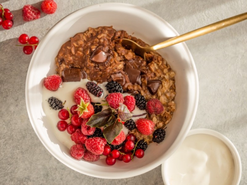 Schokoladen-Porridge in weißer Schüssel mit Obst, Draufsicht.